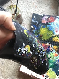 a person holding a pair of shoes with a painting on them